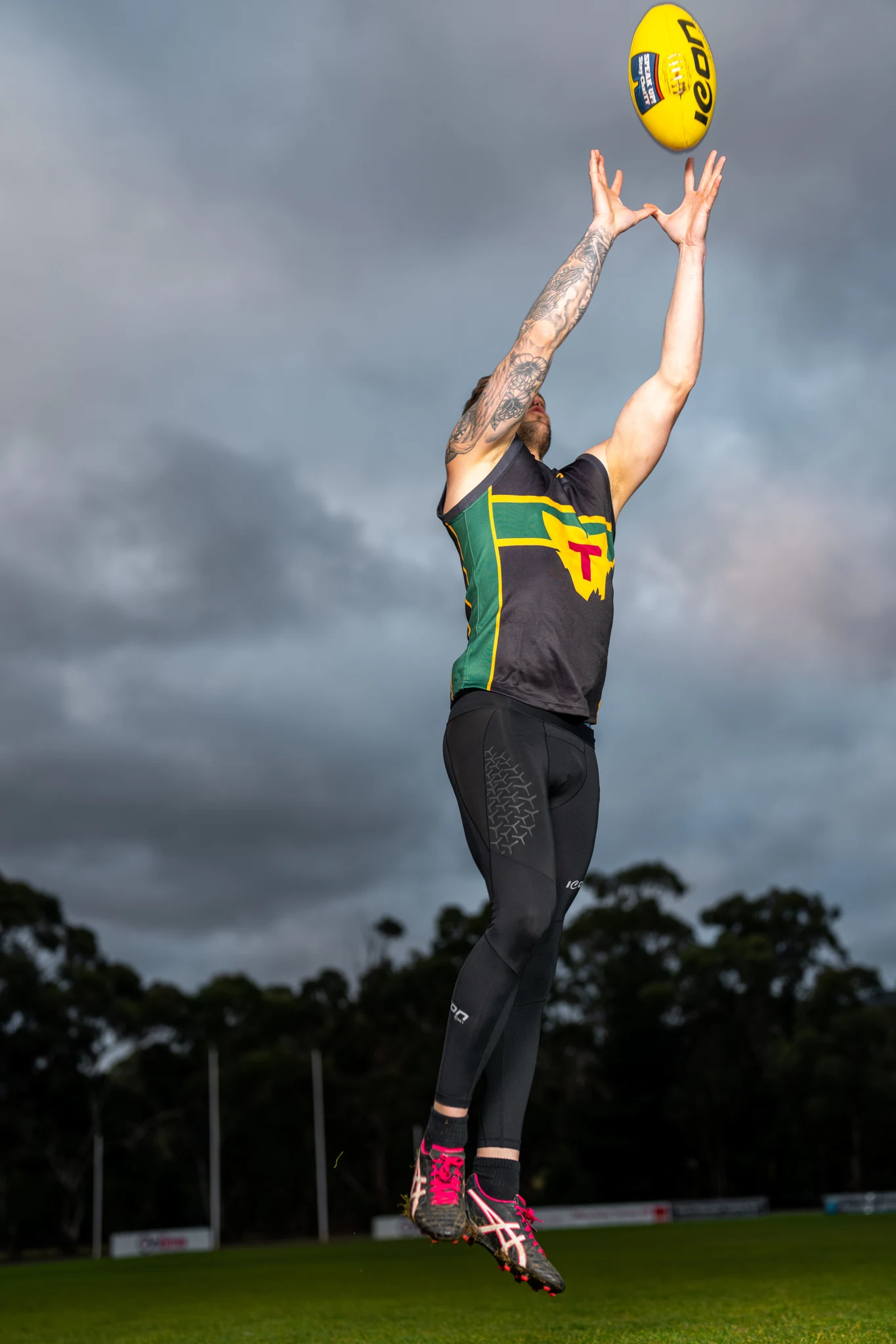 Footballer reaching for the ball in green and yellow playing kit